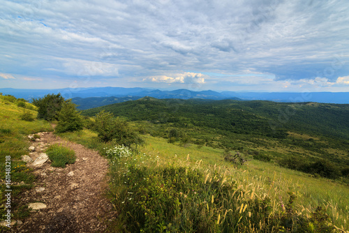 A scenic view from the hills towards Shiljak, mountain Rtanj in Serbia, showcasing lush greenery and rugged terrain under a dynamic sky.