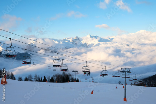 Passo Tonale, Italy - 28.01.2023: Red cable cars moving over snow-covered mountain landscape, leading to distant station building, with the snowy terrain and tracks visible below, alpine ski resort