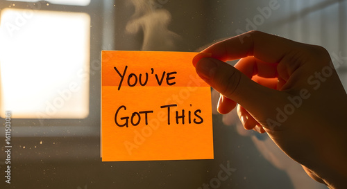 Hand holding an orange sticky note with the encouraging message 