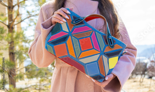 The girl holds a bag with multi-colored leather inserts in her hands