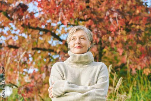Outdoor portrait of happy mature 55 - 60 year old woman in autumn park, wearing beige pullover.  Active and healthy lifestyle