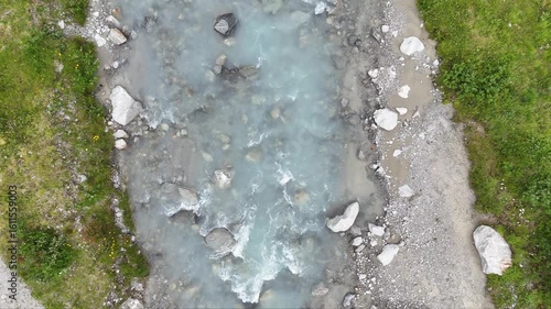 turquoise transparent glacial water flow cascade in glacier creek, rocky riverbed with sandbank framed with green summer grass, top down view, Seq. 2-2