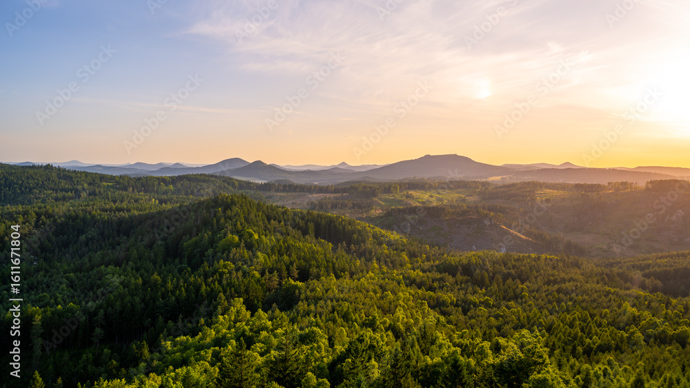 Naklejka premium A breathtaking sunset illuminates the Lusatian Mountains from the vantage point of Popov Cliffs. The landscape features lush green forests, rocky formations, and distant peaks.