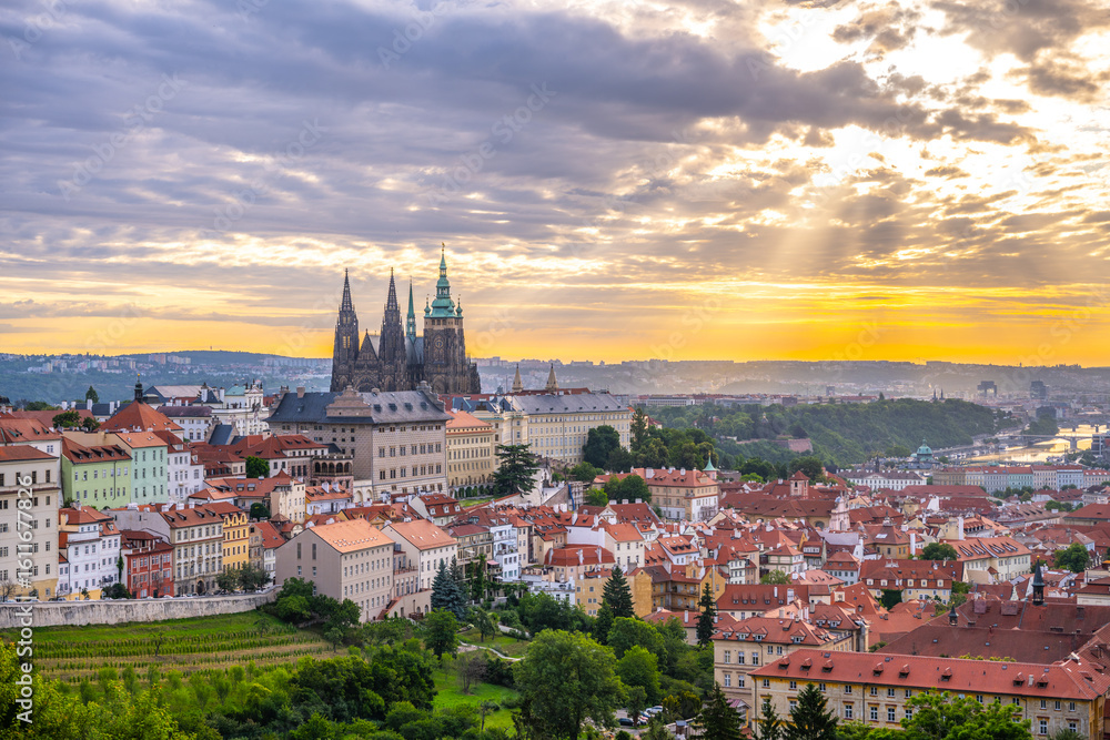 Fototapeta premium The sun rises over Prague Castle, illuminating the historic buildings and rooftops of the city. Soft clouds drift in the sky, creating a serene atmosphere in this enchanting location.
