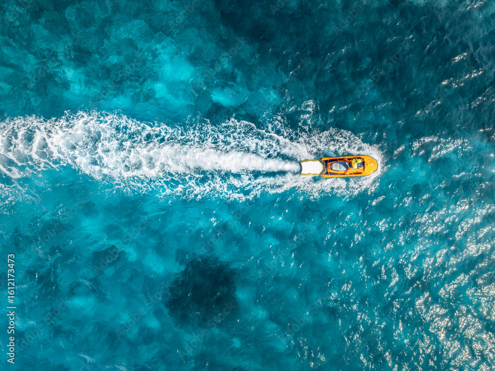 Obraz premium Aerial view of a yellow jetski sailing fast on turquoise water in Mallorca, Balearic Islands, Spain. Summer travel. Top drone view of speed boat, blue sea. Tropical seascape.