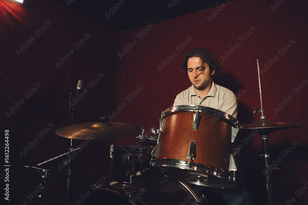 Fototapeta premium Drummer playing drums in recording studio with red background