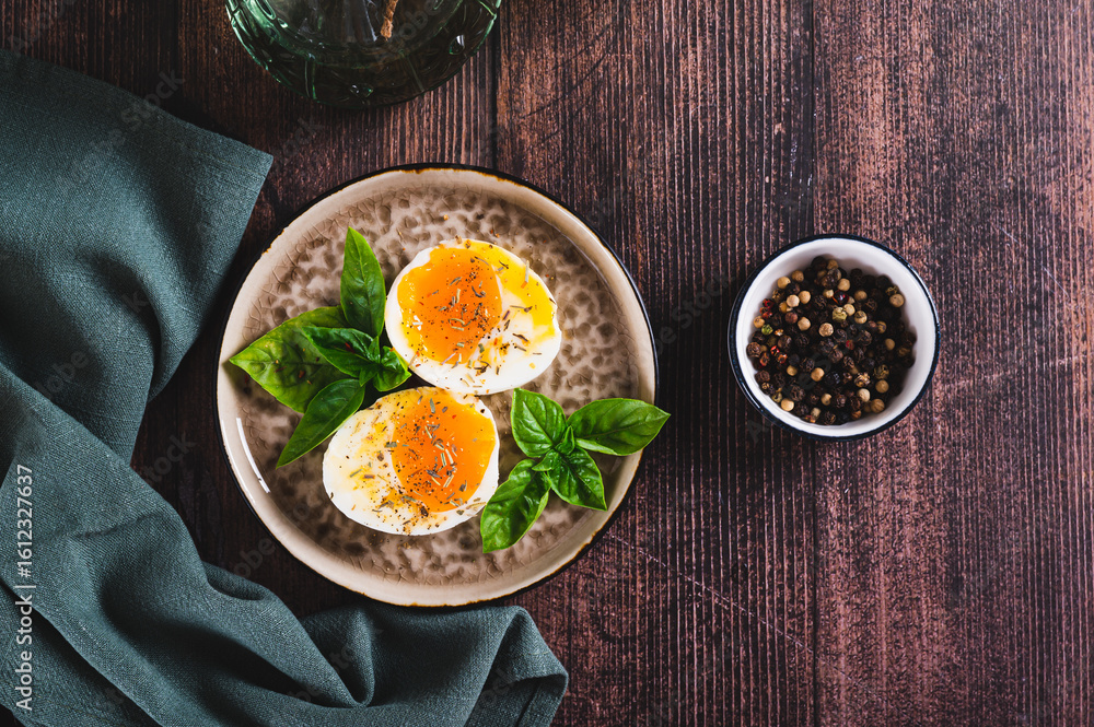 Soft-boiled egg split in half with spices and basil leaves on a plate on a table top view Soft-boiled egg split in half with spices and basil leaves on a plate on a table top view