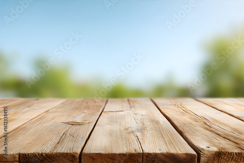Perspective view of empty wooden table with blurry green leaves and blue sky background. Concept for product display outside.