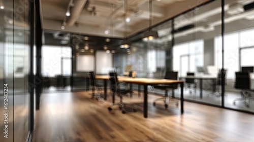 Blurred modern open-plan office interior with glass partitions, wooden flooring, dark tables, and black chairs