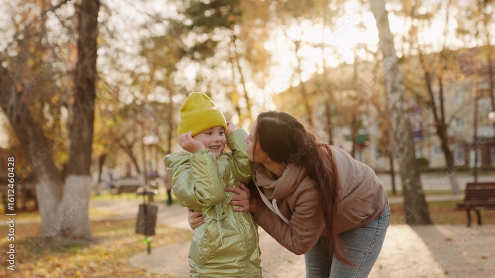 Fototapeta premium mother hugs child bright sunny park. childish smile. mother little happiness. warm day park. maternal love kid daughter. have fun together with parent autumn park yellow leaves. teamwork. laughter kid