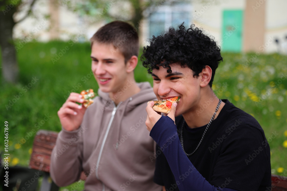 Fototapeta premium Two young guys eating pizza outdoor, picnic in park, dining outdoors