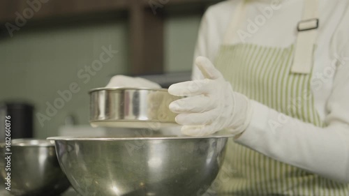 Baking in kitchen Sifting flour into mixing bowl while wearing gloves and apron, showcasing art of cooking and precise preparation for delicious treats.
