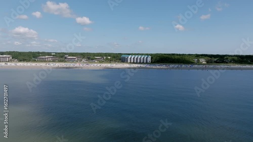 Wallpaper Mural Aerial video of Hilton Head beachfront hotels and condos along a densely occupied shoreline. The sandy beach is crowded with umbrellas and beachgoers under a clear blue sky. Torontodigital.ca