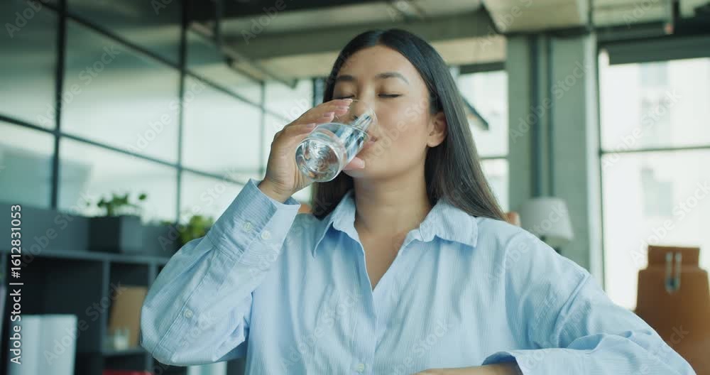 A woman enjoys a refreshing and hydrating glass of cool water in her modern office, emphasizing wellness and hydration A woman enjoys a refreshing and hydrating glass of cool water in her modern office, emphasizing wellness and hydration