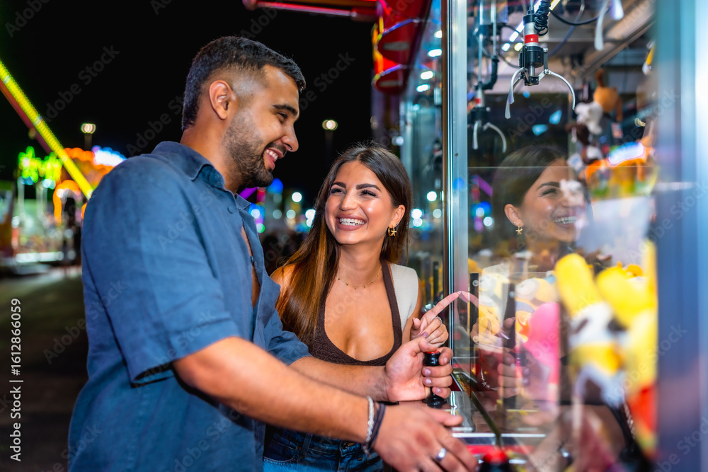 Obraz premium Happy couple playing claw crane game at amusement park at night