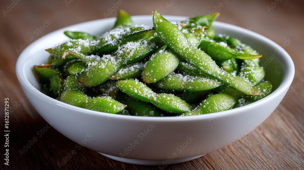 A white bowl filled with fresh green edamame beans sprinkled with sea salt. The bowl is placed on a wooden surface, highlighting the natural colors. A white bowl filled with fresh green edamame beans sprinkled with sea salt. The bowl is placed on a wooden surface, highlighting the natural colors.