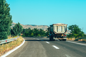 Keuken achterwand Turquoise Dump truck driving on a curvy rural road through dry countryside landscape with trees and distant hills under clear blue sky.  © Bits and Splits