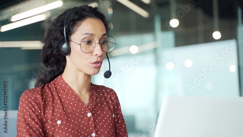 Young female corporate operator in headset working in customer support service on helpline telesale talking using laptop sitting in business office. Agent of call center advises client. Close up