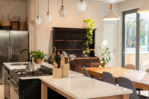 Ceramic utensil holder holding spatulas and ladles on marble island near stainless steel stove