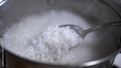 A detailed shot of a spoon lifting cooked rice from a pot of rice porridge, highlighting the soft texture and glistening grains. Perfect for recipe videos.