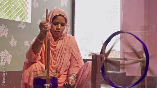 Indian woman spinning thread on a traditional hand-operated charkha. Close-up of rural textile process with colourful thread and handmade tools used for weaving and fabric making for banarasi saree