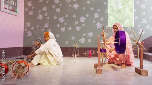 Two women work with handlooms and spinning wheels to wind colourful thread in a traditional Indian home. A scene of rural India’s textile craftsmanship and handmade weaving.