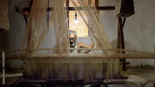 Elderly Indian man weaving on a traditional handloom in a village workshop, working with silk threads to craft handmade fabric