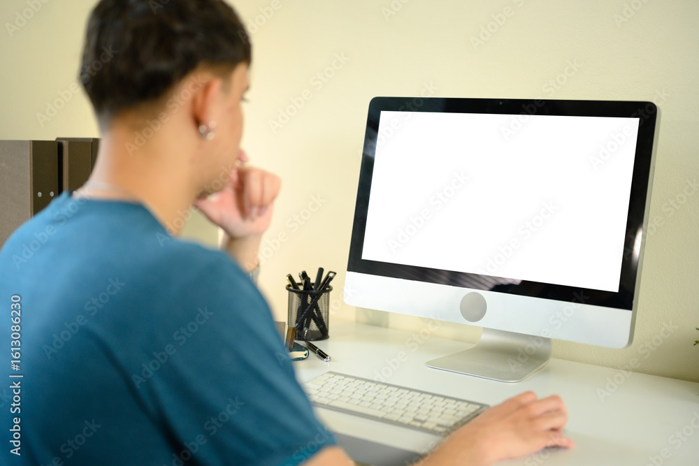 Young man working on a desktop computer at home with a blank white screen Young man working on a desktop computer at home with a blank white screen