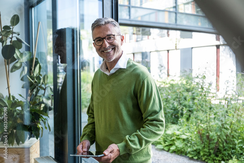 Businessperson in green sweater using tablet at office window