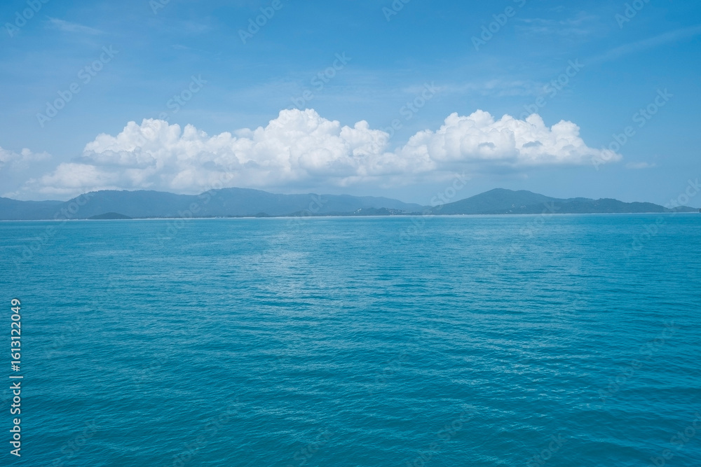 The blue sea and the background have a mountain, clouds, and clear blue sky. The blue sea and the background have a mountain, clouds, and clear blue sky.