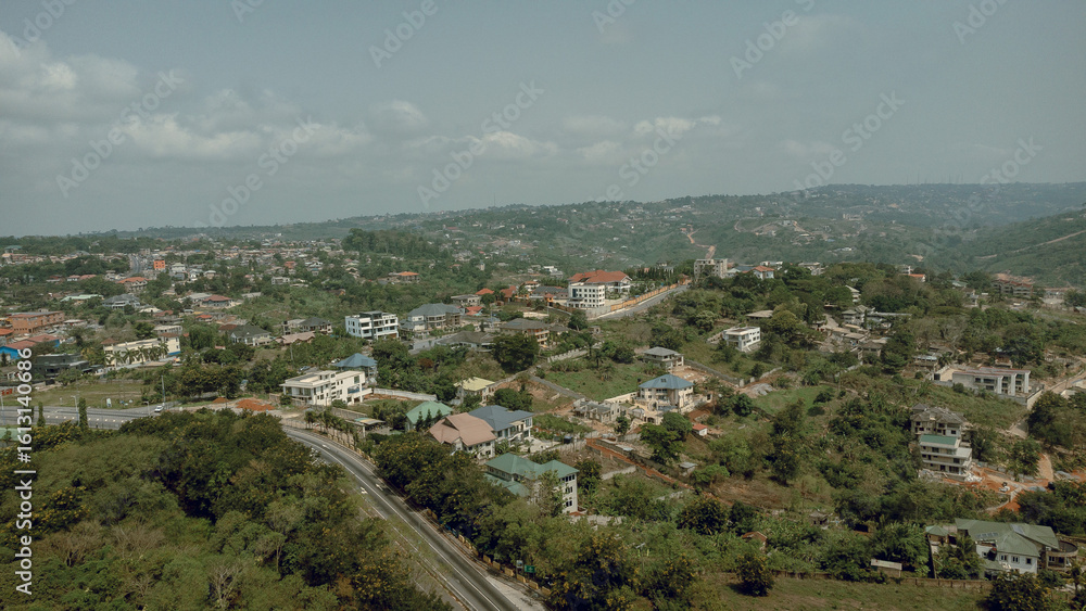 Aerial view of homes nestled among verdant trees and rolling hills under a muted sky, contrasting with the architectural details of the town, Aburi, Eastern Region, Ghana. Aerial view of homes nestled among verdant trees and rolling hills under a muted sky, contrasting with the architectural details of the town, Aburi, Eastern Region, Ghana.