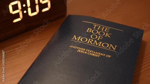 Bucharest Romania 27 July 2025. he Book of Mormon resting on a wooden nightstand beside a classic alarm clock showing 9:00 AM. Symbolic morning scene representing faith, spirituality.
