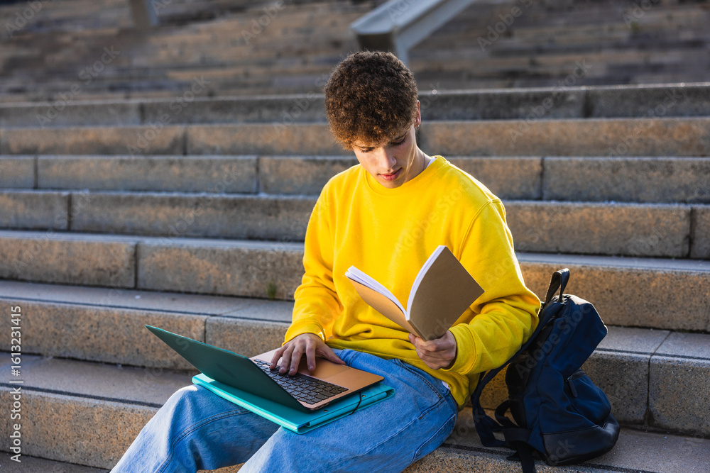 Obraz premium College student studying outdoors using laptop and textbook on stairs
