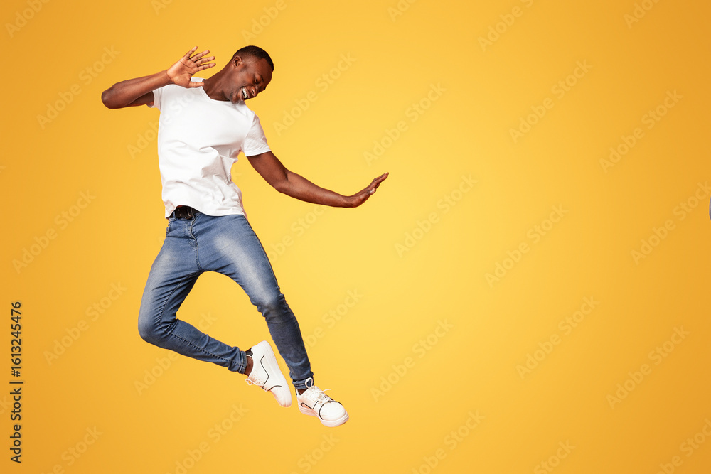 Fototapeta premium Funny black guy in casual outfit bouncing over orange studio background, full length shot. Playful african american young man expressing happiness, feeling carefree and joyful
