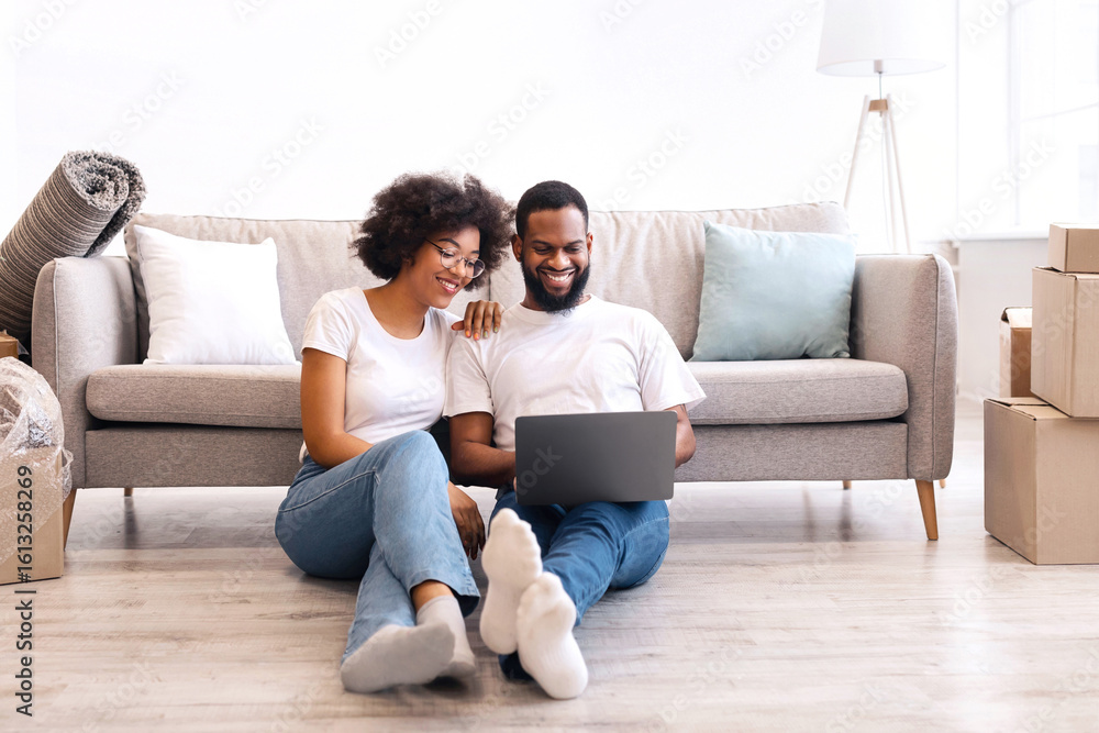 Moving House. Cheerful African American Couple Using Laptop And Browsing Internet Sitting On Floor Indoors After Relocation To New Apartment. Real Estate Ownership Concept Moving House. Cheerful African American Couple Using Laptop And Browsing Internet Sitting On Floor Indoors After Relocation To New Apartment. Real Estate Ownership Concept