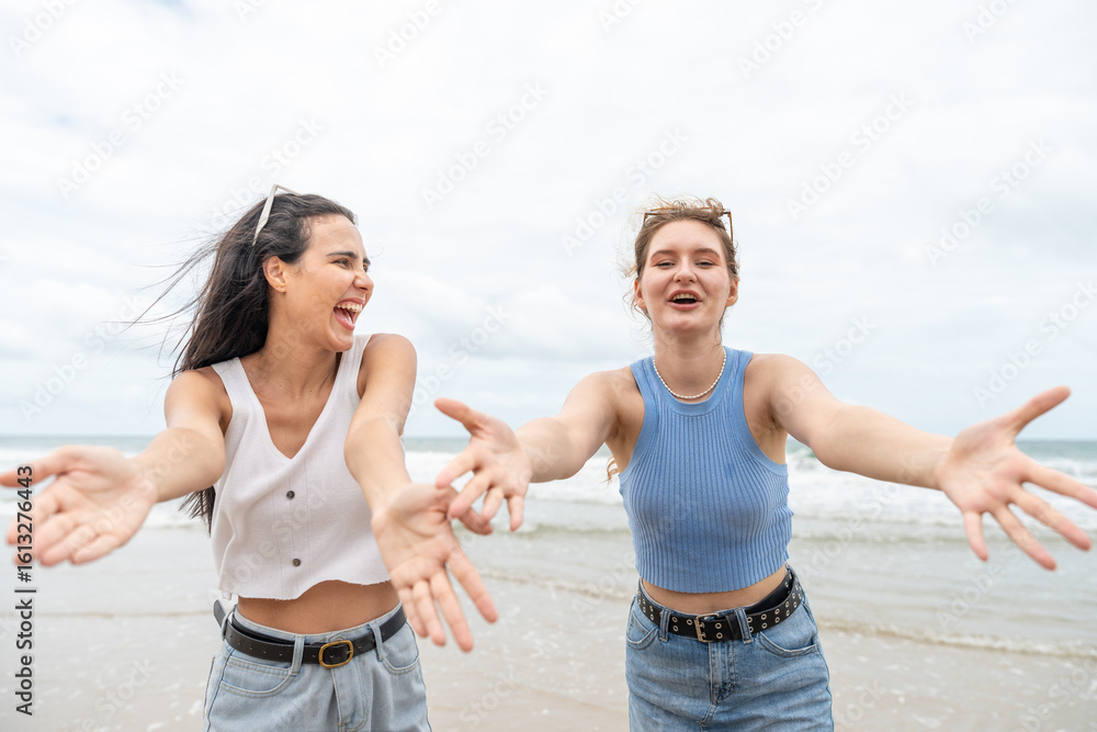 Two young women joyful arms raised and laughing together on the tropical beach. Female with friend traveling on vacation in summer Two young women joyful arms raised and laughing together on the tropical beach. Female with friend traveling on vacation in summer