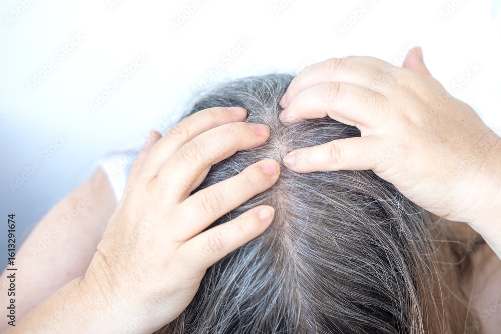 Naklejka premium Mature woman touching her gray hair, examines silver strands, deep in thought, aging process, menopause time, emotional reflection, quiet acceptance
