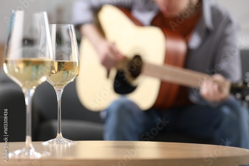 Photography Glasses with white wine on table and man playing guitar indoors, selective focus