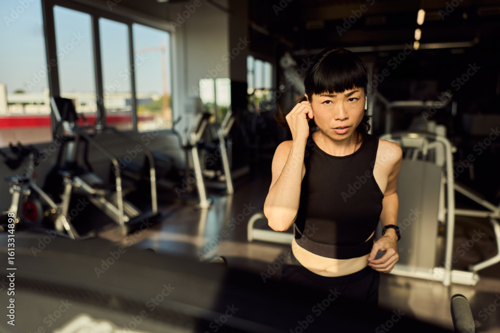 Fototapeta premium Focused Woman Running on a Treadmill in a Modern Fitness Gym
