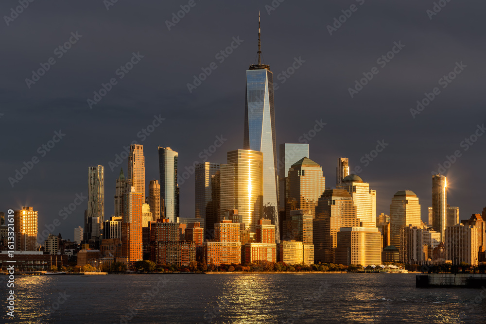 Fototapeta premium Skyscrapers of the World Trade Center complex at sunset, seen from across the Hudson River. Lower Manhattan skyline glowing in warm light, New York City