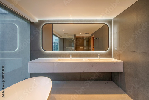 Modern luxury bathroom with a backlit mirror, double sink marble vanity, and dark grey tiles. High-end real estate interior design.