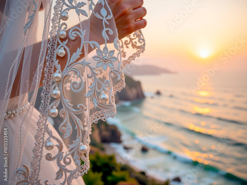 Bride holding wedding veil while standing by the ocean at sunset  
