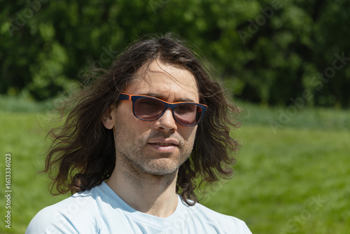Portrait of glasses brunette man feeling unwell, depression, unhappy at park and green nature setting.