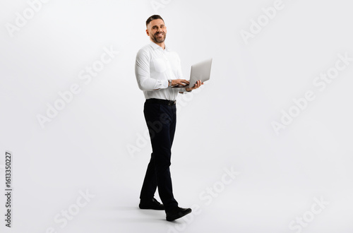 Full length shot of businessman with laptop walking over light grey studio background, male entrepreneur using computer for remote work or online shopping, free space
