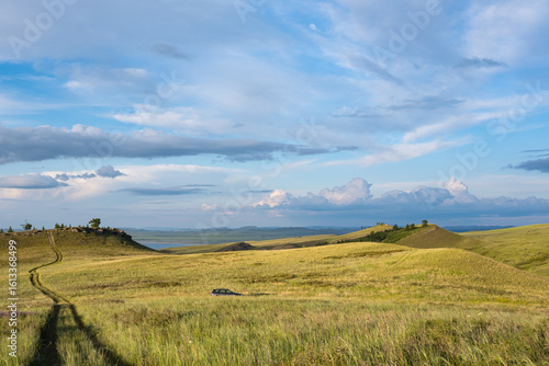 Beautiful sunset light in the evening, in a hilly steppe area in Siberia. A car in a field in the middle, the sky in the clouds