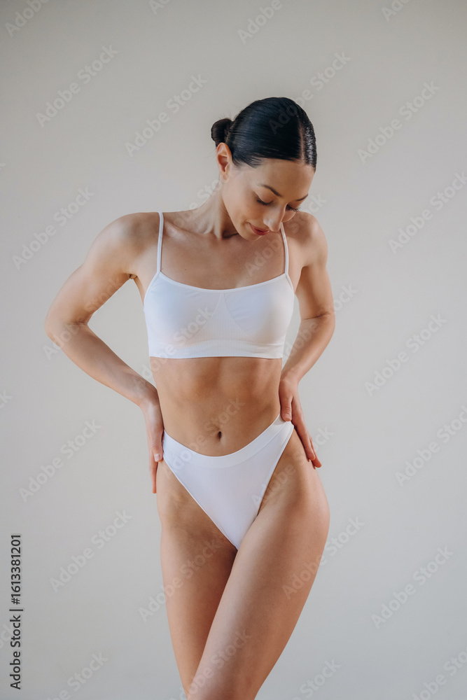 Obraz premium White creamy background. Young woman in sportive clothes is against the wall