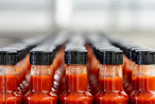 Many bottles of hot sauce waiting on conveyor belt in food processing plant