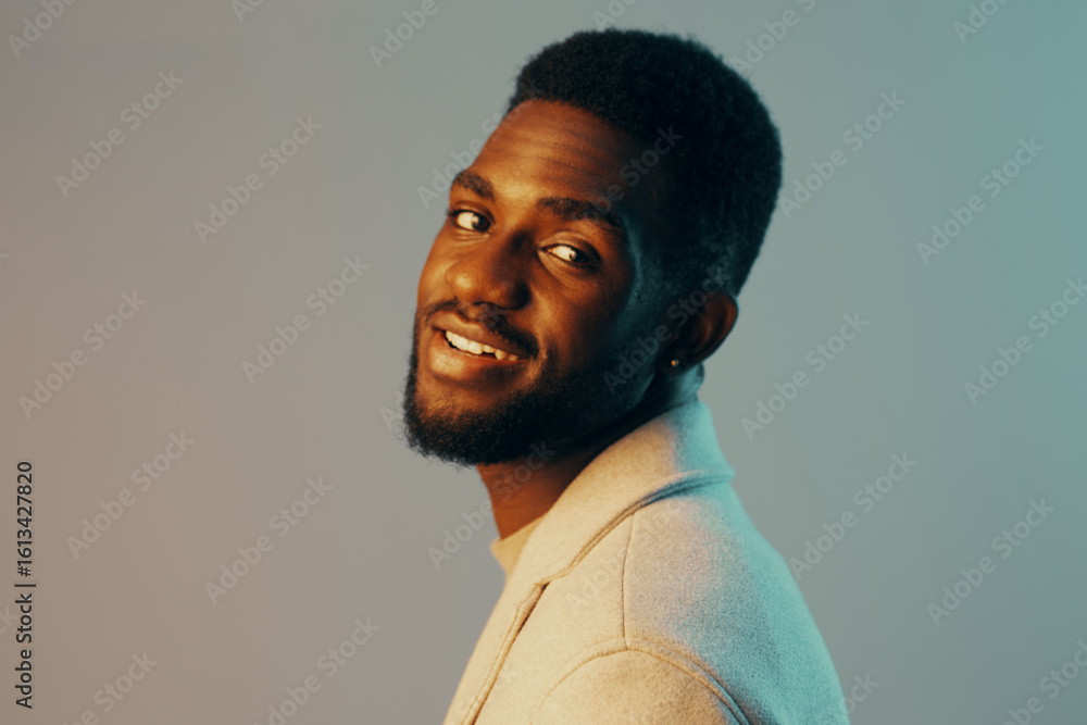 Obraz premium A cheerful Black man in a stylish light sweater smiles confidently against a soft gradient background, embodying warmth and creativity in a modern portrait