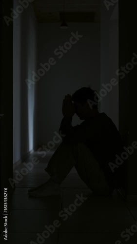 Despair and sadness young man praying alone in dark hallway feeling loss disappointment and hopelessness. Vertical video