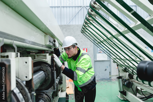 Engineer at cardboard plant performs quality control check on industrial equipment, emphasizing safety protocols and smooth operation of production systems.
